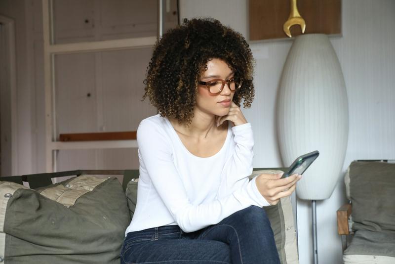 Mujer en el sofá de casa revisando su factura en el móvil